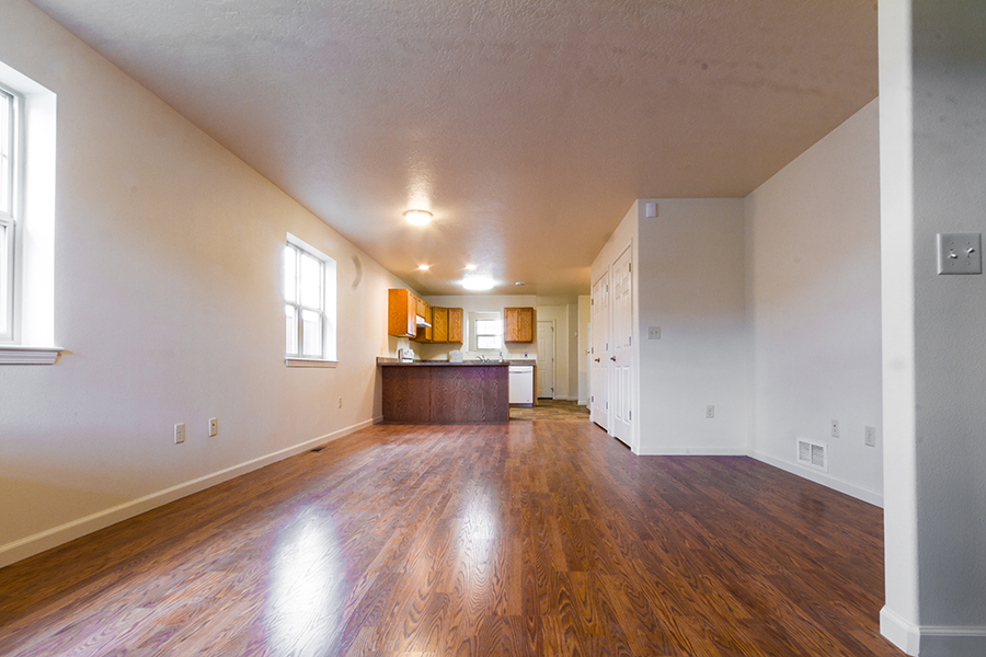 A picture shows the length of the inside of the home, from the front door across the open, wood-floored living room, linoleum-tiled kitchen all the way to the back door.